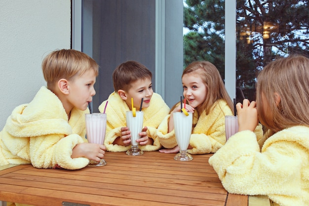 Free photo large group of friends taking goog time with milk cocktails. happy smiling boys and girs in yellow terry dressing gowns. kids fashion concept