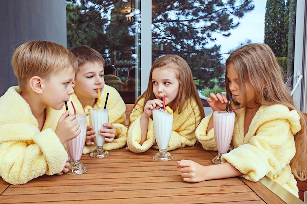 Free photo large group of friends taking goog time with milk cocktails. happy smiling boys and girs in yellow terry dressing gowns. kids fashion concept