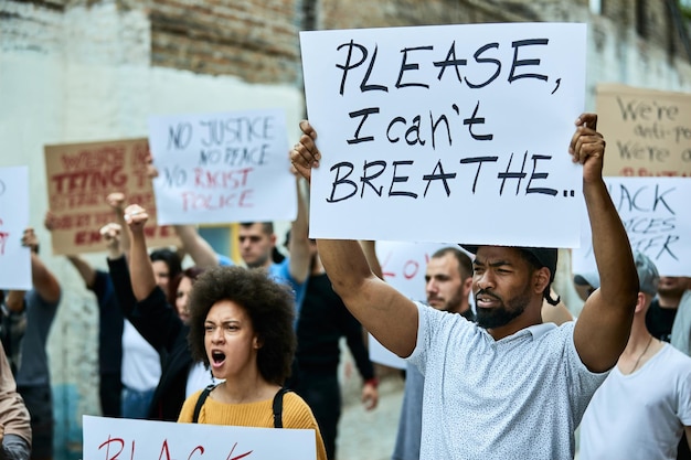 Free photo large group of people on a black lives matter protest focus is on black man holding a placard with please i can't breathe inscription