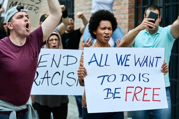 Free photo large group of people demonstrating against racism on the streets focus is on black woman carrying placard with freedom inscription