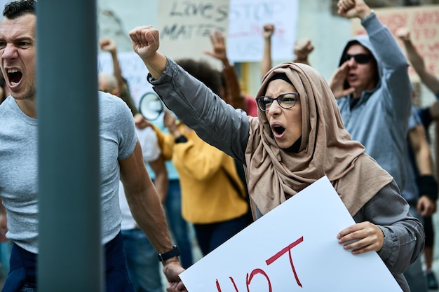 Large multiethnic group of people protesting against racism on the streets Focus is on angry Middle Eastern woman shouting with raised fist