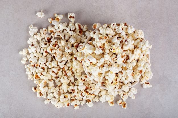 Large pile of popcorn completely covering a bowl on marble.