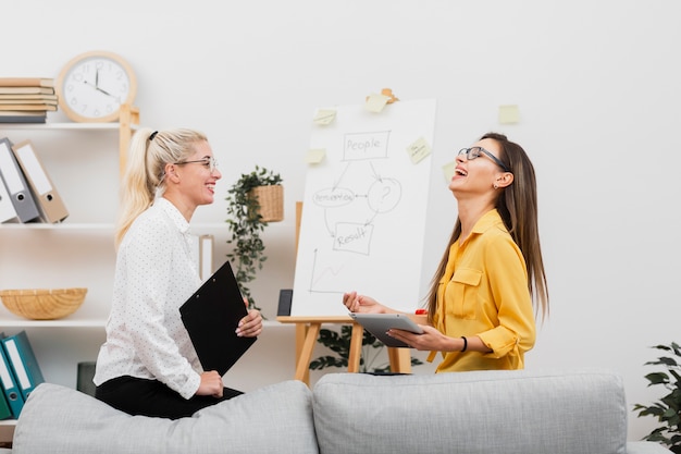 Free Photo lateral view smiling women holding a tablet and a clipboard