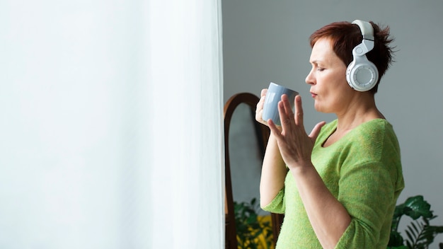 Lateral view woman listening music and holding a mug