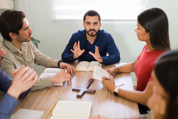 Latin man in his 20s with a lot of faith explaining the holy scriptures to young men and women part of a religious community