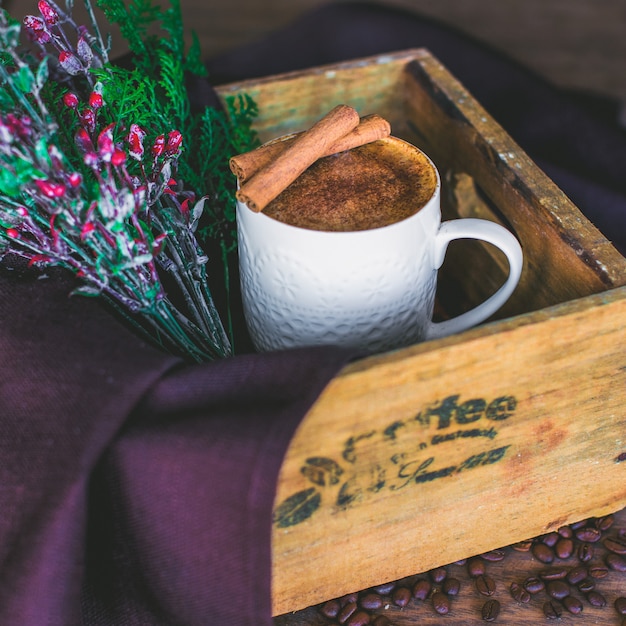 Latte cup garnished with cinnamon sticks served in wood box with tree branch