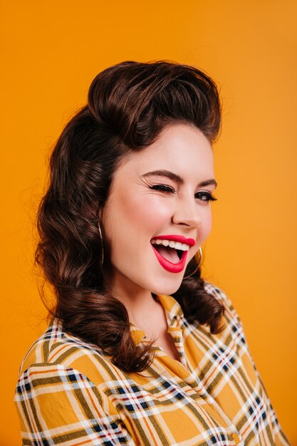 Laughing brunette woman posing on yellow background. Portrait of smiling pinup girl in checkered shirt.