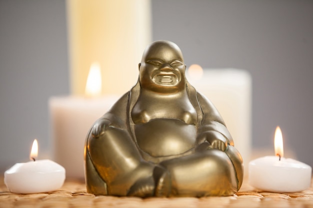 Free photo laughing buddha figurine and lit candles on mat