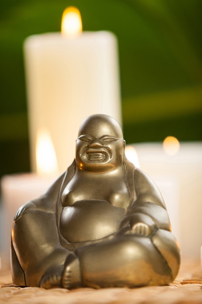 Free photo laughing buddha figurine and lit candles on mat