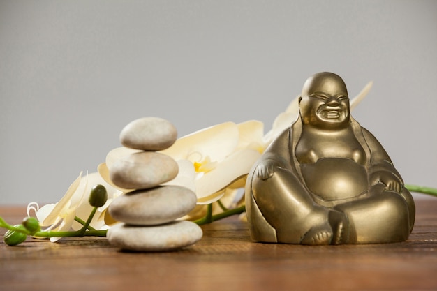 Free photo laughing buddha figurine with pebbles stone and flower