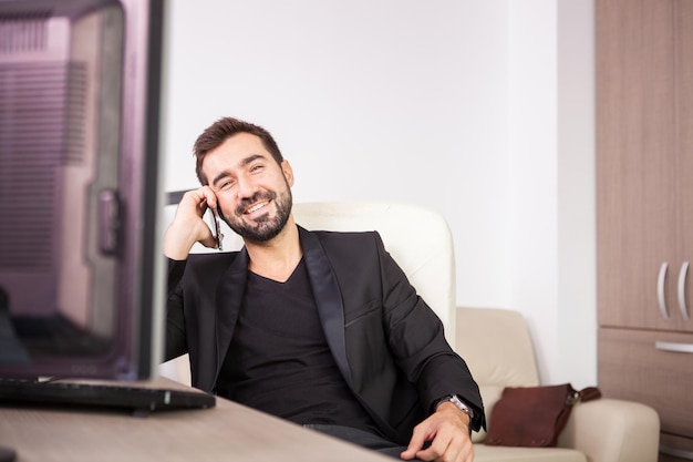 Laughing Businessman talking on the phone while working in his office. Businessperson in professional environment