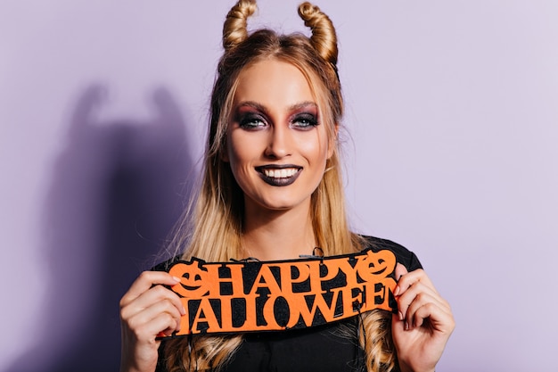 Free Photo laughing female model with dark halloween makeup posing on purple wall. indoor photo of pretty blonde girl.