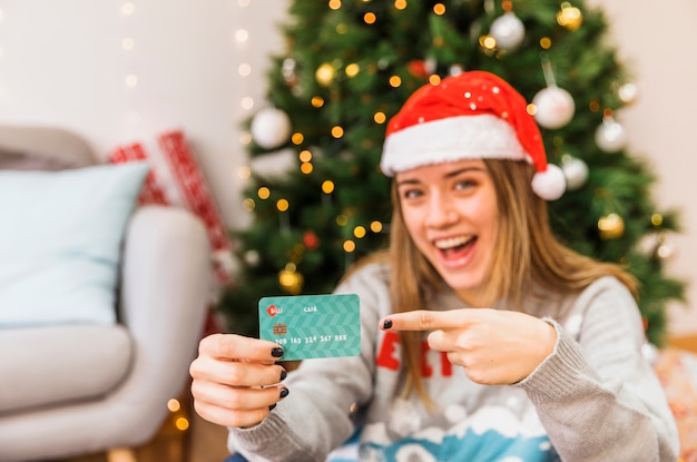 Laughing festive woman pointing at credit card 