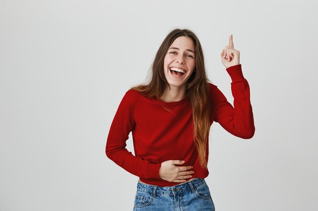 Laughing happy attractive woman, touching belly and pointing finger up