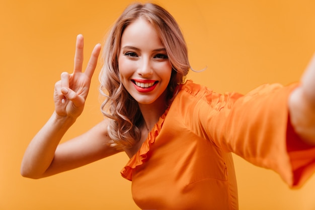 Free photo laughing joyful woman in orange dress taking picture of herself