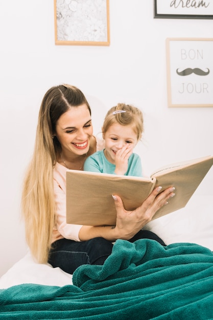 Free photo laughing mother and daughter reading book on bed