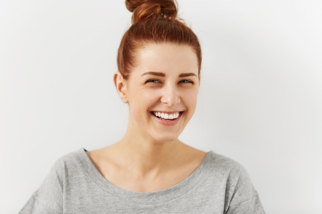 Laughing out loud. Close up shot of attractive cheerful young woman wearing her ginger hair in bun squinting eyes mocking at something funny or ridiculous while relaxing indoors. People and lifestyle