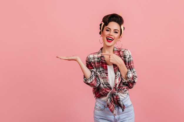 Laughing pinup girl posing with hand up. Studio shot of fashionable caucasian lady isolated on pink background.