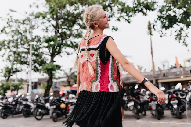 Free photo laughing woman with long blonde braids. outdoor shot of graceful tanned woman wears colorful knitted clothes.