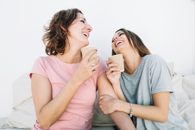 Laughing women drinking hot beverages on sofa