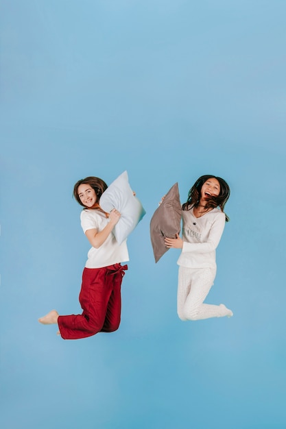 Free photo laughing women jumping with pillows