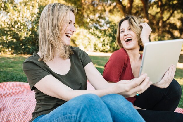 Laughing women using tablet in park