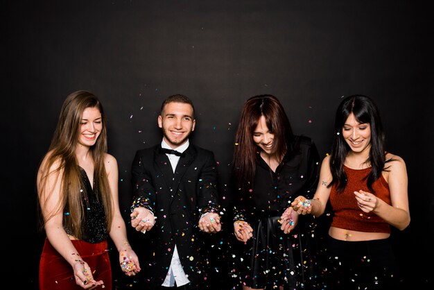 Laughing young women and man in evening cloths tossing confetti