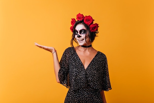 Laughing zombie lady posing on yellow background. Stunning female model in mexican halloween attire smiling to camera.