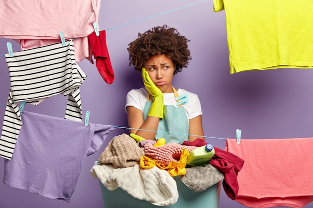 Free photo laundry day concept. fatigue dissatisfied woman touches cheek and looks away in unhappiness