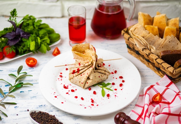 Lavash snack roll with cheese and grenate seeds, bread, vegetables and sorbet on a white plate. Snack 