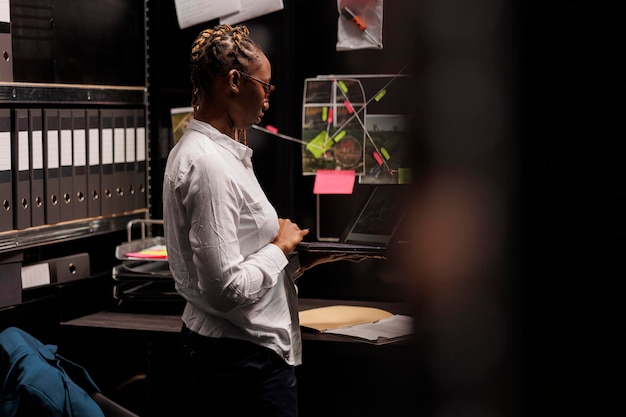 Free photo lawyer preparing for case in police detective office, studying investigation file. african american woman law enforcement standing near desk and reading forensic expertise report