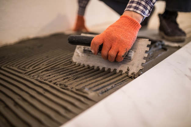 Free Photo laying ceramic tiles. troweling mortar onto a concrete floor in preparation for laying white floor tile.