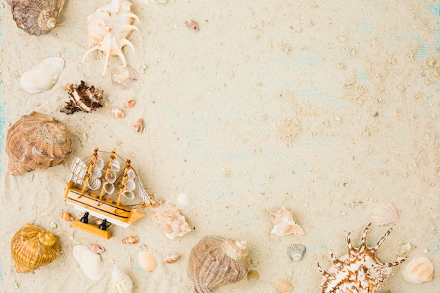 Free photo layout of seashells and toy boat on sand