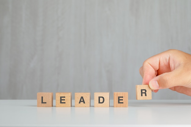 Free photo leadership concept on grey and white table side view. hand picking up wooden cube.