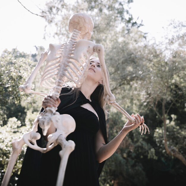 Leaning lady in witch costume holding skeleton