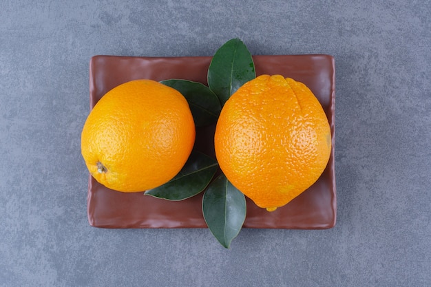 Leaves and juicy oranges on wooden plate plate on marble table.