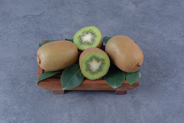 Leaves and kiwi on wooden plate on marble table.