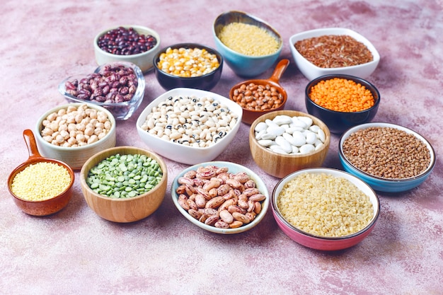 Legumes and beans assortment in different bowls on light stone surface . Top view. Healthy vegan protein food.