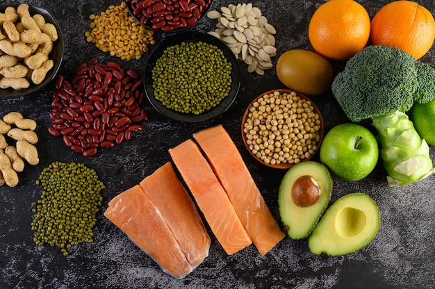 Legumes, broccoli, fruit, and salmon placed on a black cement floor.