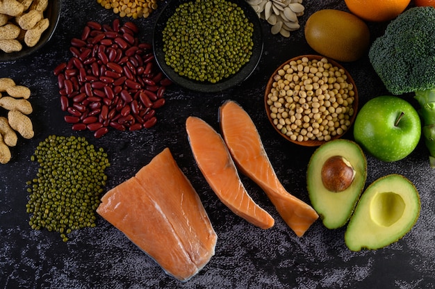 Legumes, broccoli, fruit, and salmon placed on a black cement floor.