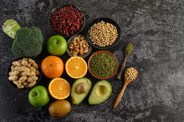 Legumes and fruit on a black cement floor surface.