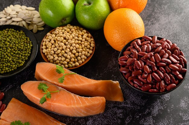 Legumes, fruit, and salmon placed on a black cement floor.