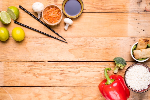 Lemon; chopsticks; mushroom; sauces; bell peppers; broccoli; rice and spring rolls on wooden plank