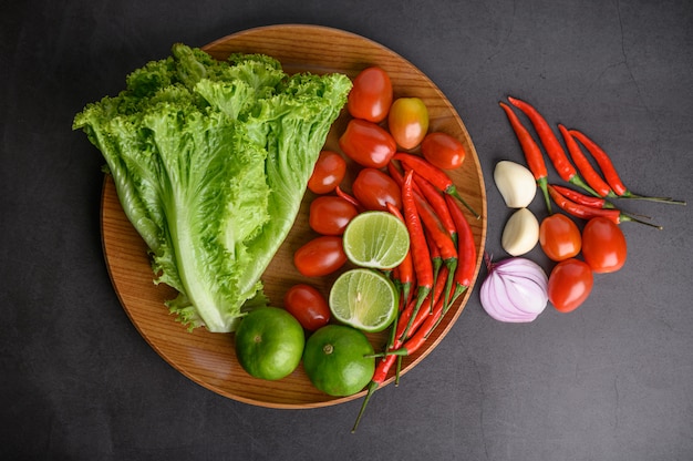 Lemon slice, shallots, garlic, tomatoes, lettuce and peppers on a wooden plate on a black cement floor.