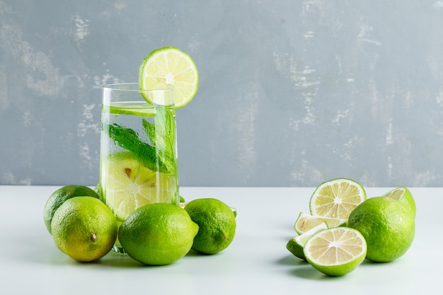 Lemonade in a glass with lemons, herbs side view on white and plaster