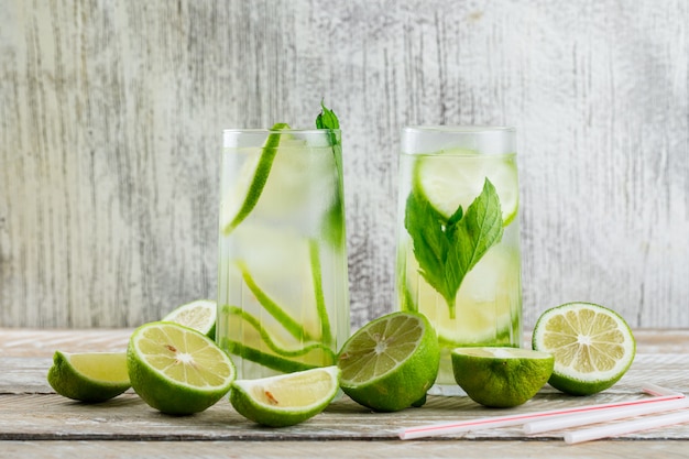 Lemonade in glasses with lemon, basil, straws side view on wooden and grungy