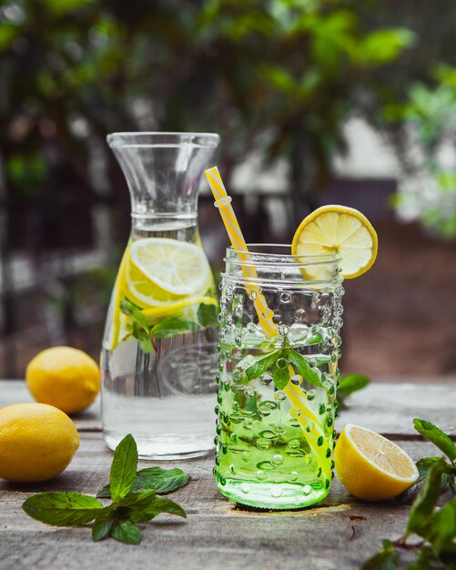 Lemonade and ingredients in glass jug and jar on wooden and garden table. side view.