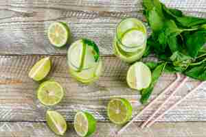 Free photo lemonade with lemon, basil, straws in glasses on wooden, flat lay.