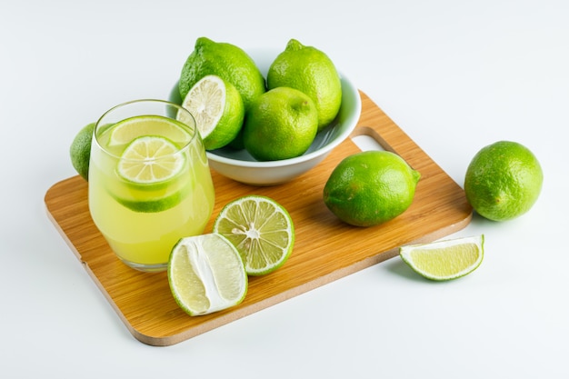 Lemonade with lemons in a glass on white and cutting board, high angle view.