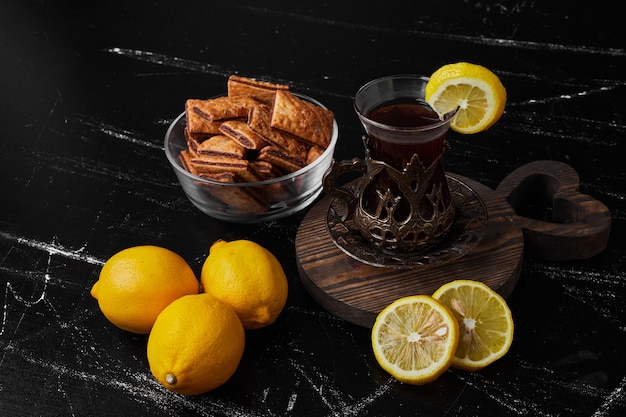 Lemons isolated on a black surface with tea and pastries.